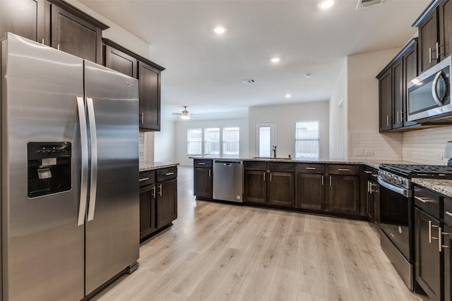 kitchen featuring stainless steel appliances, light stone countertops, decorative backsplash, kitchen peninsula, and light wood-type flooring