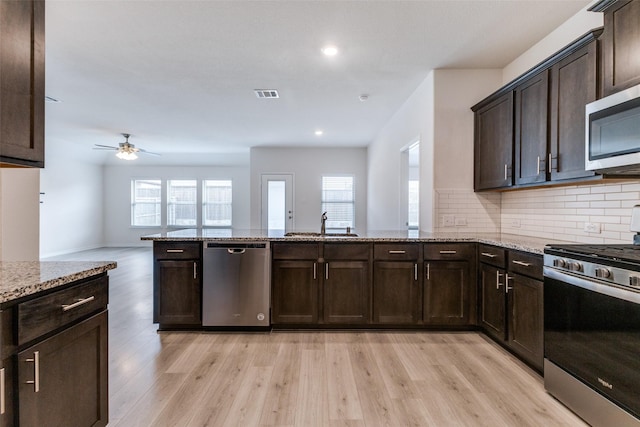 kitchen with decorative backsplash, appliances with stainless steel finishes, light stone countertops, and light hardwood / wood-style flooring