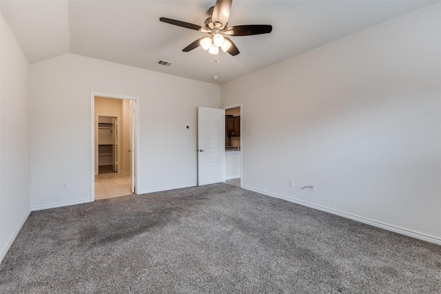 unfurnished bedroom featuring ceiling fan, vaulted ceiling, a walk in closet, light colored carpet, and a closet