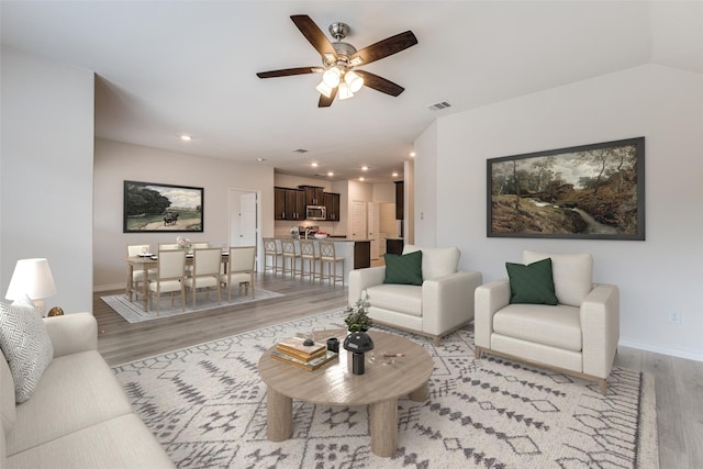 living room featuring light hardwood / wood-style flooring, ceiling fan, and vaulted ceiling