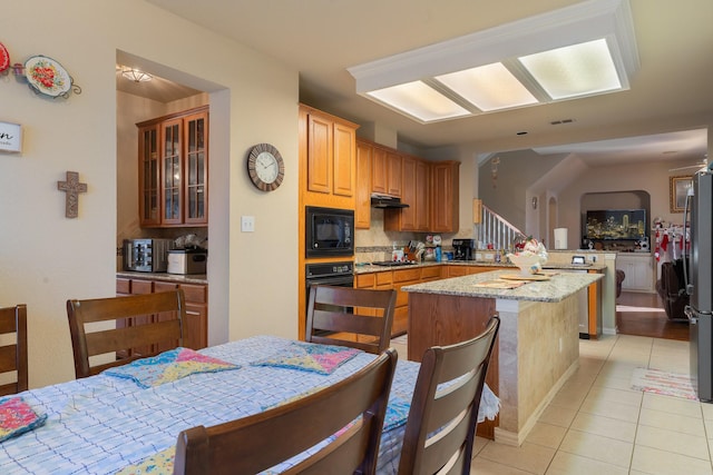 kitchen with light tile patterned floors, backsplash, light stone countertops, a kitchen island, and black appliances