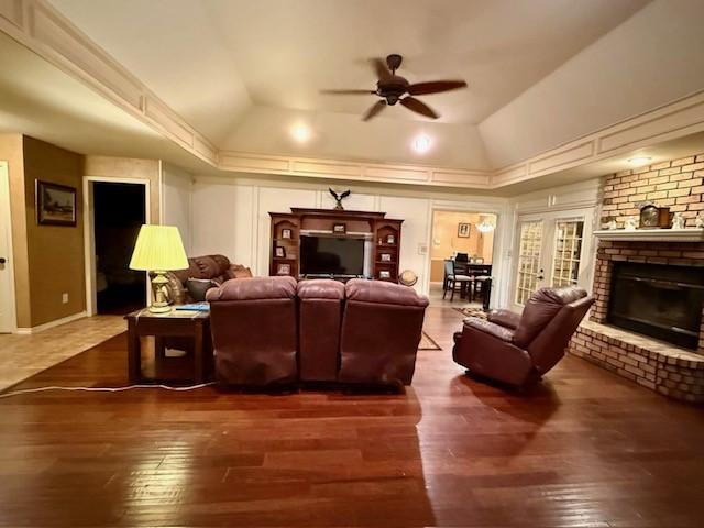 living room featuring lofted ceiling, a brick fireplace, a tray ceiling, and dark wood-type flooring