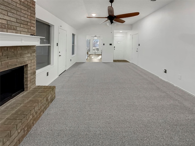 unfurnished living room featuring ceiling fan, vaulted ceiling, a brick fireplace, and carpet flooring