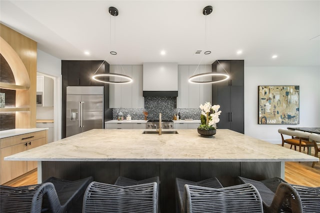 kitchen featuring hanging light fixtures, a kitchen island with sink, and built in refrigerator