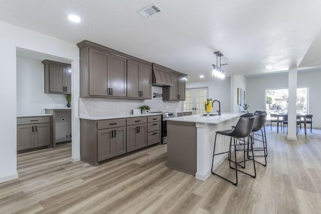 kitchen featuring stainless steel range with electric stovetop, an island with sink, hanging light fixtures, light hardwood / wood-style flooring, and sink