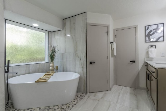 bathroom featuring a tub to relax in, vanity, and tile walls