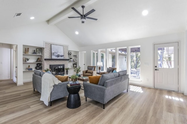 living room featuring ceiling fan, a fireplace, beamed ceiling, and light wood-type flooring