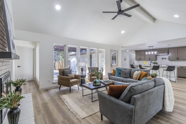 living room featuring light hardwood / wood-style floors, a brick fireplace, ceiling fan, high vaulted ceiling, and beamed ceiling