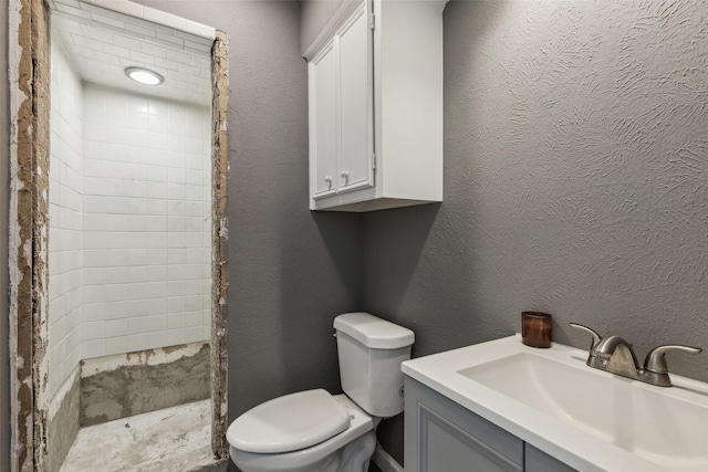 bathroom featuring toilet, vanity, and tiled shower