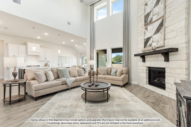 living room with a towering ceiling, sink, a stone fireplace, and light hardwood / wood-style floors