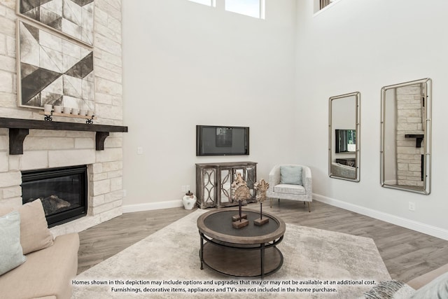 living room featuring hardwood / wood-style flooring, a towering ceiling, and a stone fireplace