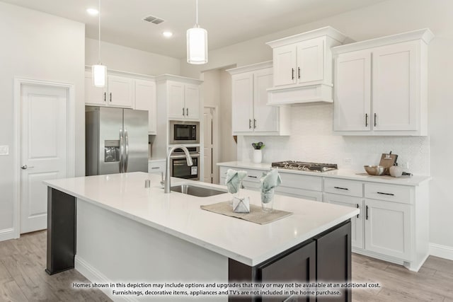 kitchen featuring white cabinetry, a center island with sink, appliances with stainless steel finishes, decorative light fixtures, and light wood-type flooring