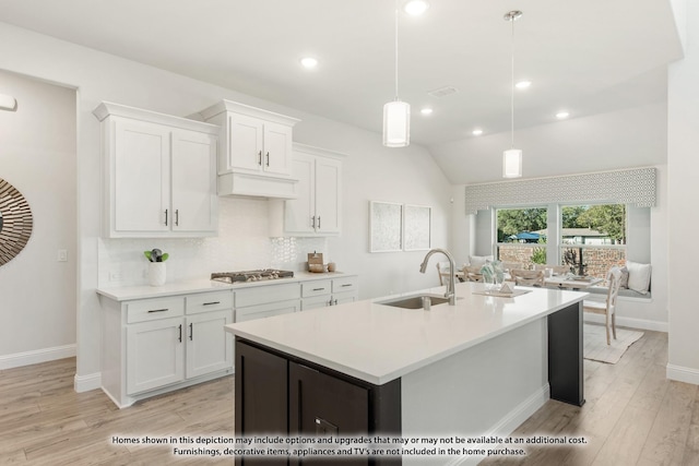 kitchen with decorative light fixtures, lofted ceiling, stainless steel gas stovetop, sink, and white cabinetry