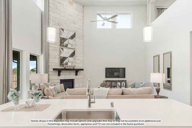 living room featuring a high ceiling, a wealth of natural light, sink, and a stone fireplace