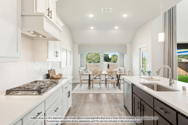 kitchen featuring appliances with stainless steel finishes, lofted ceiling, decorative light fixtures, white cabinetry, and sink