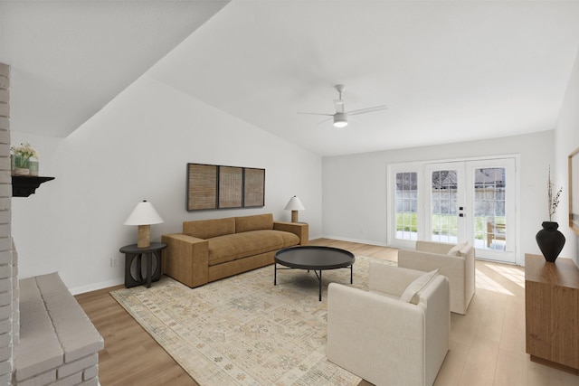 living area with ceiling fan, lofted ceiling, french doors, a fireplace, and light wood-style floors