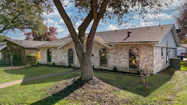 view of front facade with brick siding, central AC, a front yard, and roof with shingles