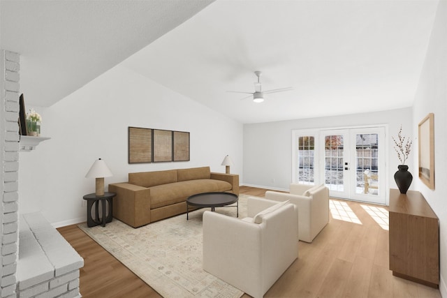 living room featuring ceiling fan, lofted ceiling, a brick fireplace, light wood-type flooring, and french doors