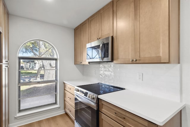 kitchen with tasteful backsplash, stainless steel appliances, light wood-style floors, brown cabinetry, and light countertops