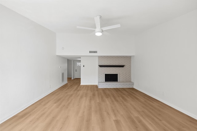 unfurnished living room with ceiling fan, a brick fireplace, and light hardwood / wood-style floors