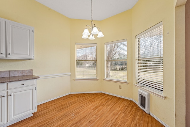 unfurnished dining area featuring heating unit, an inviting chandelier, and light hardwood / wood-style floors