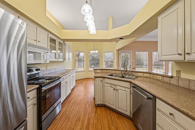 kitchen with light hardwood / wood-style floors, appliances with stainless steel finishes, a notable chandelier, hanging light fixtures, and sink