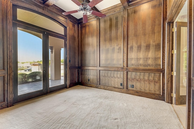 carpeted spare room with ceiling fan, wooden walls, coffered ceiling, french doors, and beamed ceiling