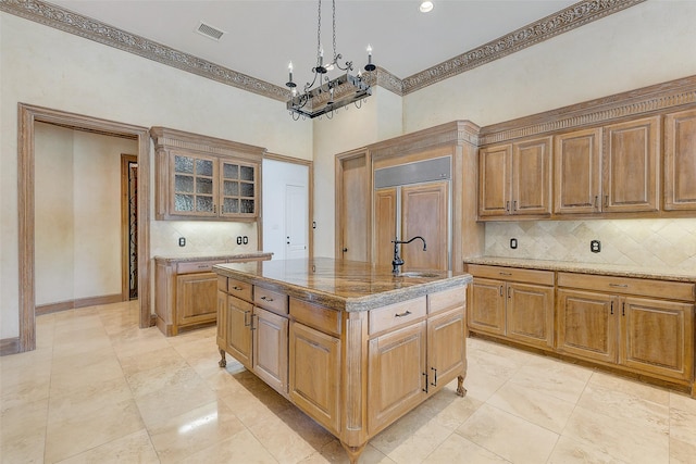 kitchen featuring sink, backsplash, hanging light fixtures, paneled built in refrigerator, and a center island with sink