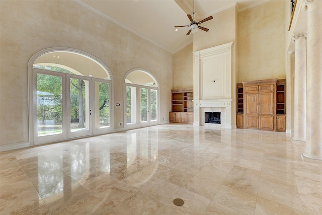 unfurnished living room featuring ornamental molding, ceiling fan, a premium fireplace, decorative columns, and a high ceiling