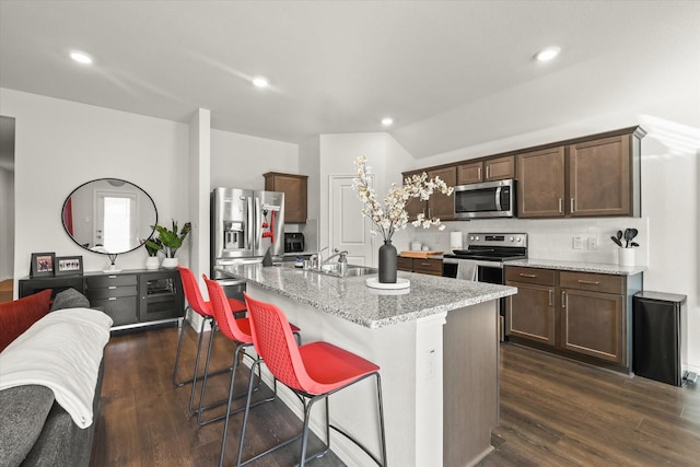 kitchen featuring an island with sink, appliances with stainless steel finishes, decorative backsplash, light stone counters, and sink