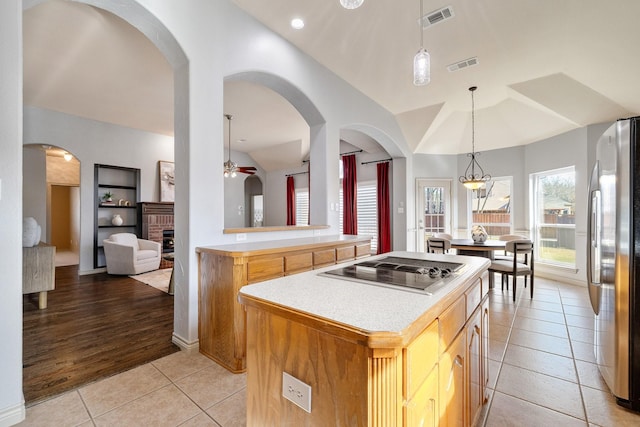 kitchen with black electric stovetop, a brick fireplace, light tile patterned flooring, stainless steel refrigerator, and a center island