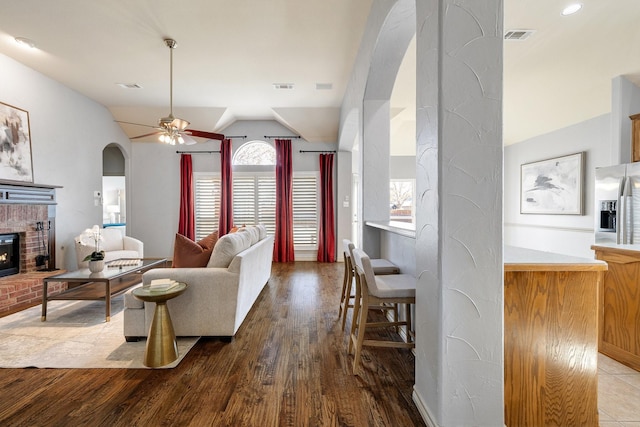 living room featuring ceiling fan, vaulted ceiling, a fireplace, and light hardwood / wood-style floors