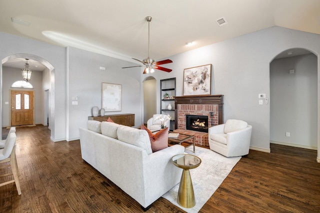 living room featuring dark wood-type flooring, ceiling fan, a brick fireplace, and lofted ceiling