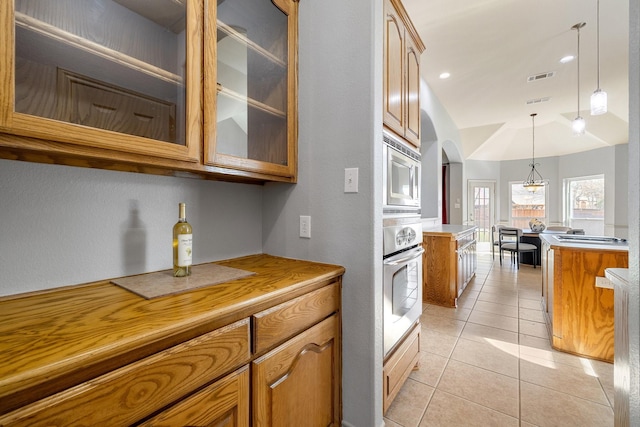 kitchen featuring light tile patterned floors, stainless steel appliances, decorative light fixtures, vaulted ceiling, and a kitchen island