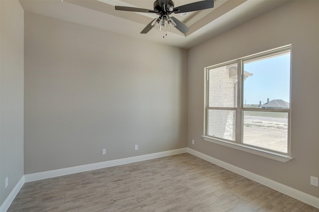 unfurnished room featuring light wood-type flooring, ceiling fan, and a tray ceiling