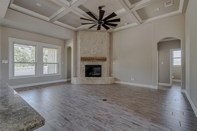 unfurnished living room featuring ceiling fan, beamed ceiling, a stone fireplace, and coffered ceiling