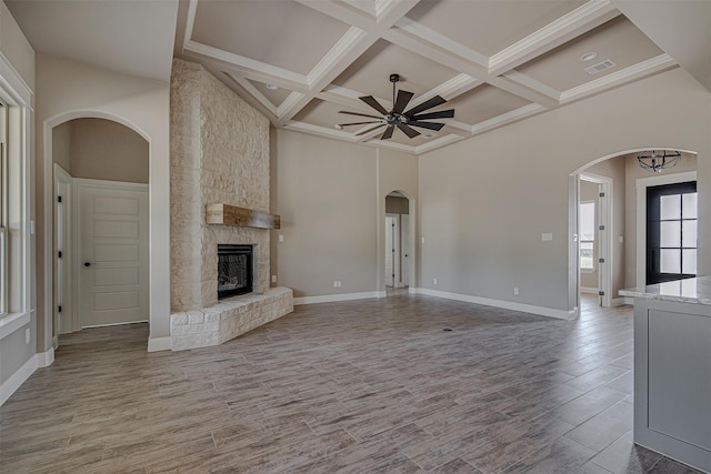 unfurnished living room with a towering ceiling, beamed ceiling, a fireplace, ceiling fan, and coffered ceiling