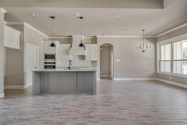 kitchen featuring pendant lighting, custom exhaust hood, white cabinetry, a kitchen island with sink, and appliances with stainless steel finishes