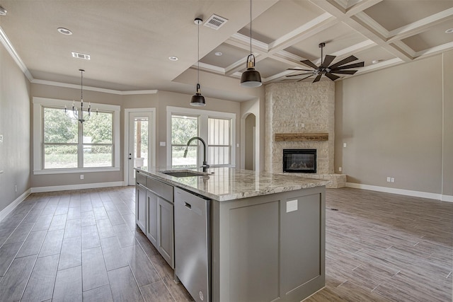 kitchen featuring dishwasher, sink, coffered ceiling, light stone countertops, and an island with sink