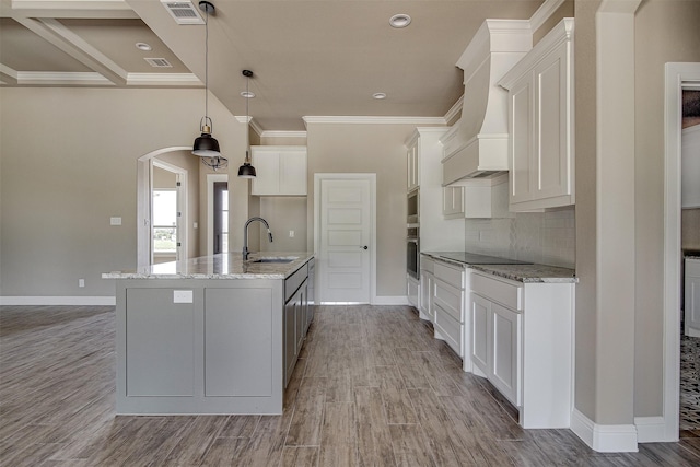 kitchen with decorative light fixtures, white cabinetry, sink, a kitchen island with sink, and stainless steel oven