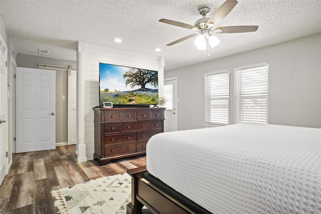 bedroom featuring ceiling fan, a barn door, dark hardwood / wood-style flooring, and a textured ceiling