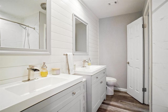 bathroom featuring toilet, vanity, wood-type flooring, and a tile shower