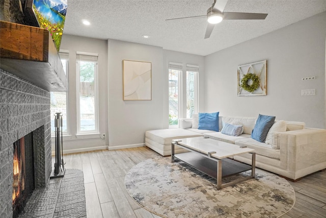 living room with hardwood / wood-style flooring, a brick fireplace, ceiling fan, a textured ceiling, and a wealth of natural light