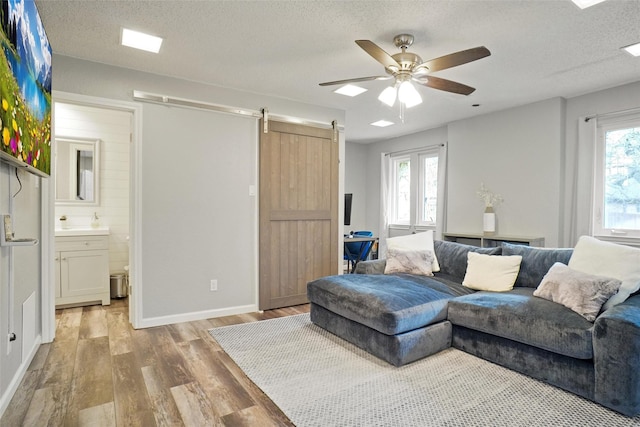 living room with light wood-type flooring, ceiling fan, a textured ceiling, and a barn door