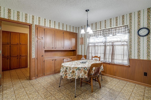 dining room with a textured ceiling, a chandelier, and wooden walls