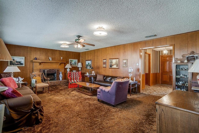 living room with a brick fireplace, a textured ceiling, carpet floors, and ceiling fan