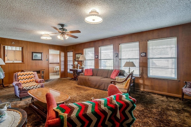 living room featuring ceiling fan, wood walls, and dark carpet