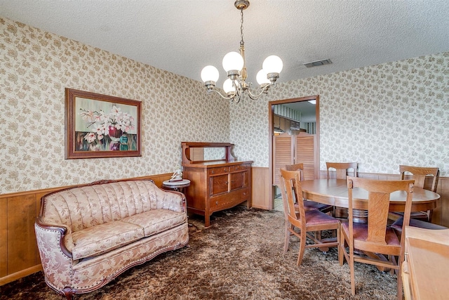 dining area with dark carpet, wooden walls, an inviting chandelier, and a textured ceiling