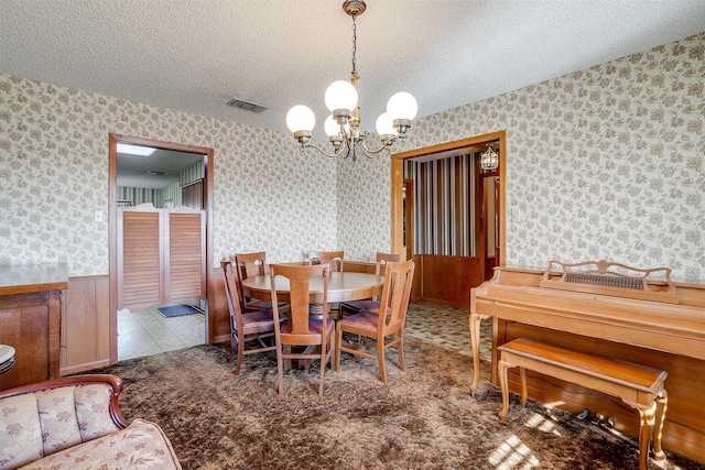 dining space with wooden walls, an inviting chandelier, and a textured ceiling