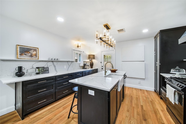 kitchen with range, light hardwood / wood-style floors, a kitchen breakfast bar, hanging light fixtures, and a kitchen island with sink